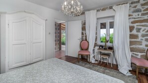 A bedroom with a large bed, a chandelier, a stone wall, and a window with curtains. - Beach front home in Rab (Rab)