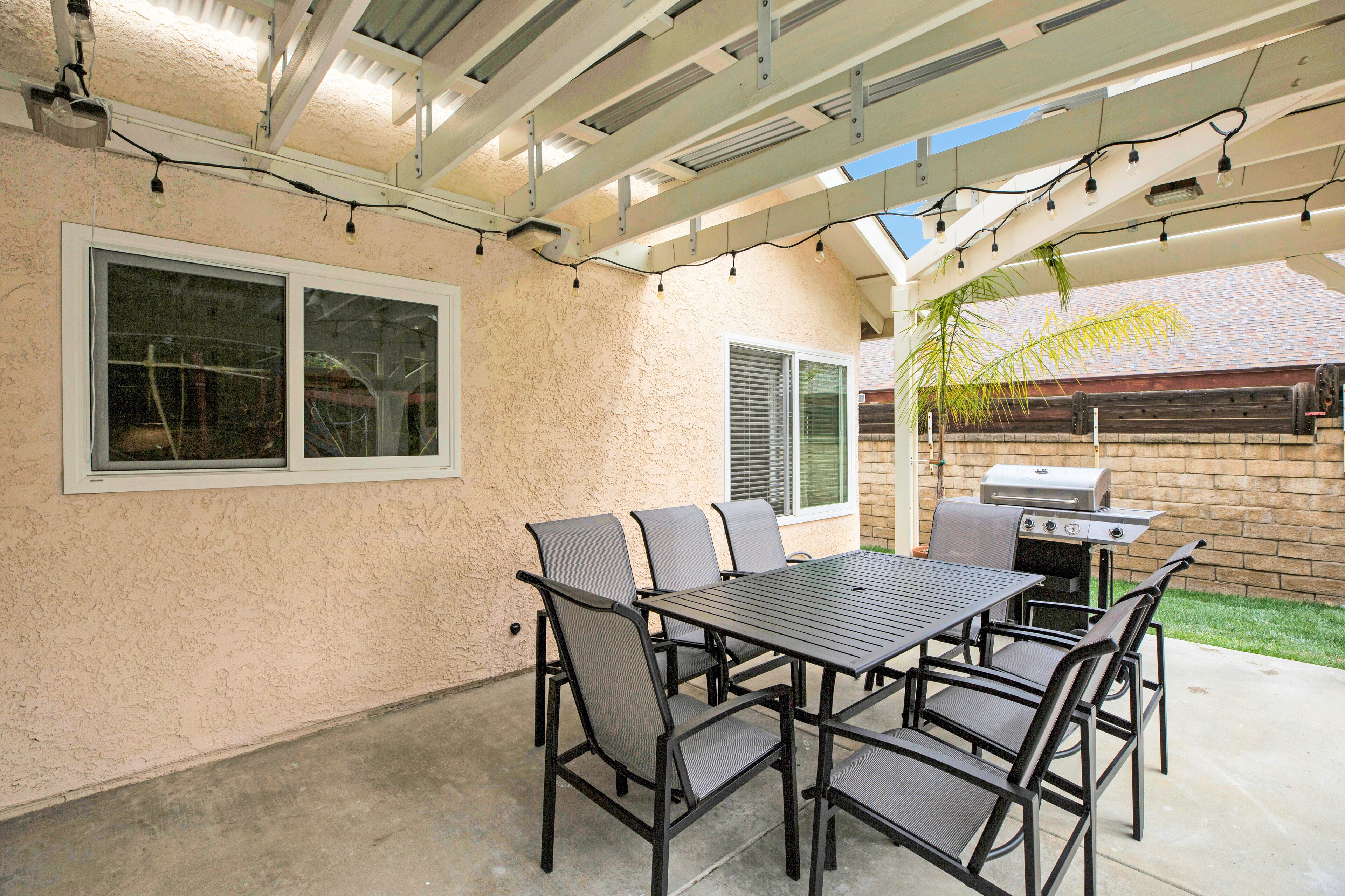 An outdoor patio with a table and chairs, a grill, and string lights.