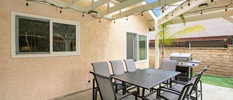 An outdoor patio with a table and chairs, a grill, and string lights.