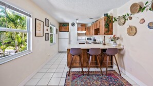 A kitchen with a large window, wooden bar stools, and a patterned rug. - Charming Bungalow w/ Pool in North Palm Beach (West Palm Beach)