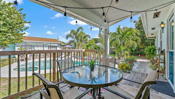 A covered outdoor patio with a glass table and chairs, overlooking a swimming pool and lush greenery. - Charming Bungalow w/ Pool in North Palm Beach (West Palm Beach)