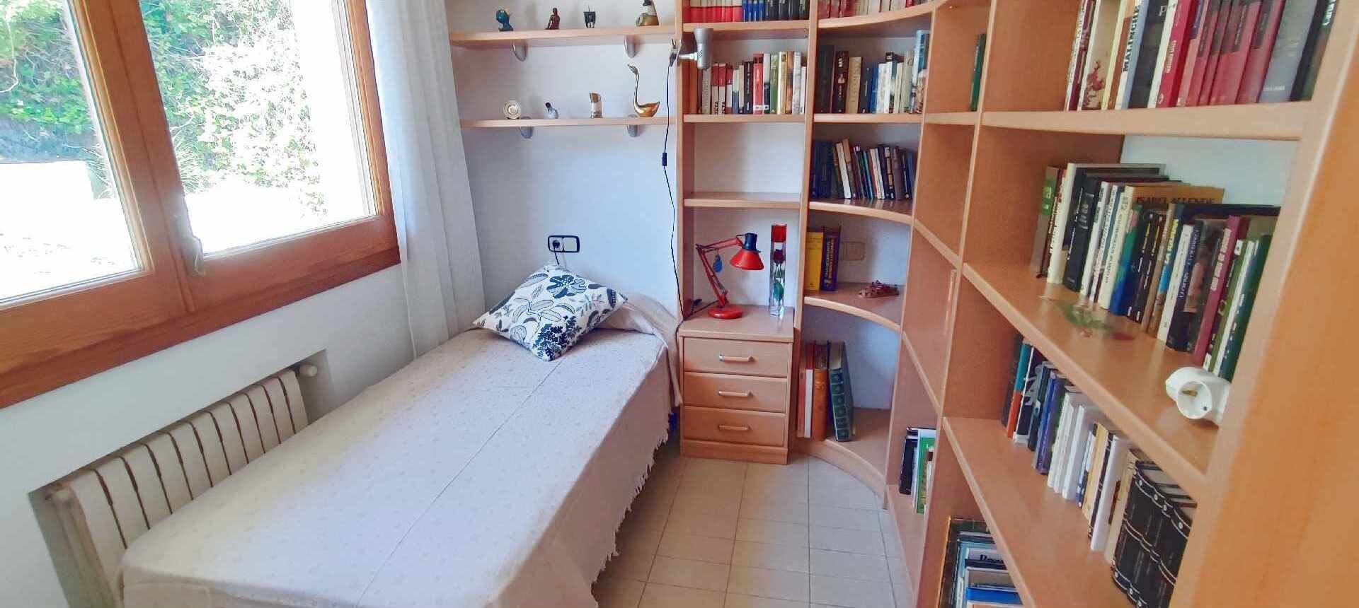Ein kleines Schlafzimmer mit einem Einzelbett, einem Nachttisch, einem Bücherregal und einem Fenster.