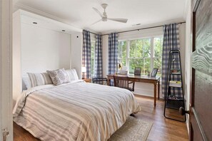 A bedroom with a bed, a desk, and a window with curtains.