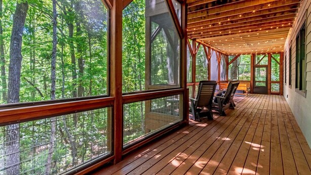 Une véranda couverte avec de grandes fenêtres, un plancher en bois et une vue sur une forêt.