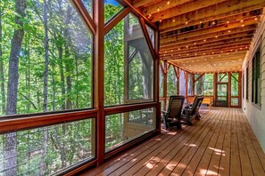 Un porche cubierto con amplios ventanales, suelo de madera y vistas a un bosque.