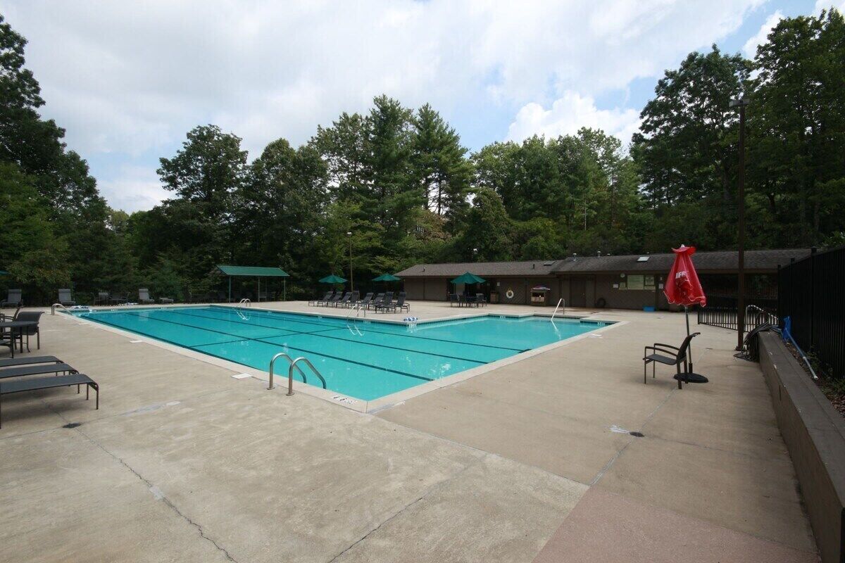 Une piscine rectangulaire dotée de plusieurs couloirs de nage, entourée de chaises longues et de parasols, avec des arbres en arrière-plan.