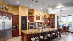 Una cocina con isla central, armarios de madera oscura, electrodomésticos de acero inoxidable e iluminación colgante.