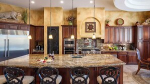 Una cocina con una isla grande, armarios de madera oscura, electrodomésticos de acero inoxidable y una cabeza de leopardo decorativa en la pared.