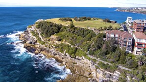 Une propriété située sur la côte, avec un rivage rocheux, une zone herbeuse et un bâtiment doté de plusieurs balcons donnant sur la mer.