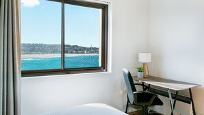 Une chambre d’hôtel avec un lit, un bureau doté d’une lampe et une vue sur la plage et la ville.