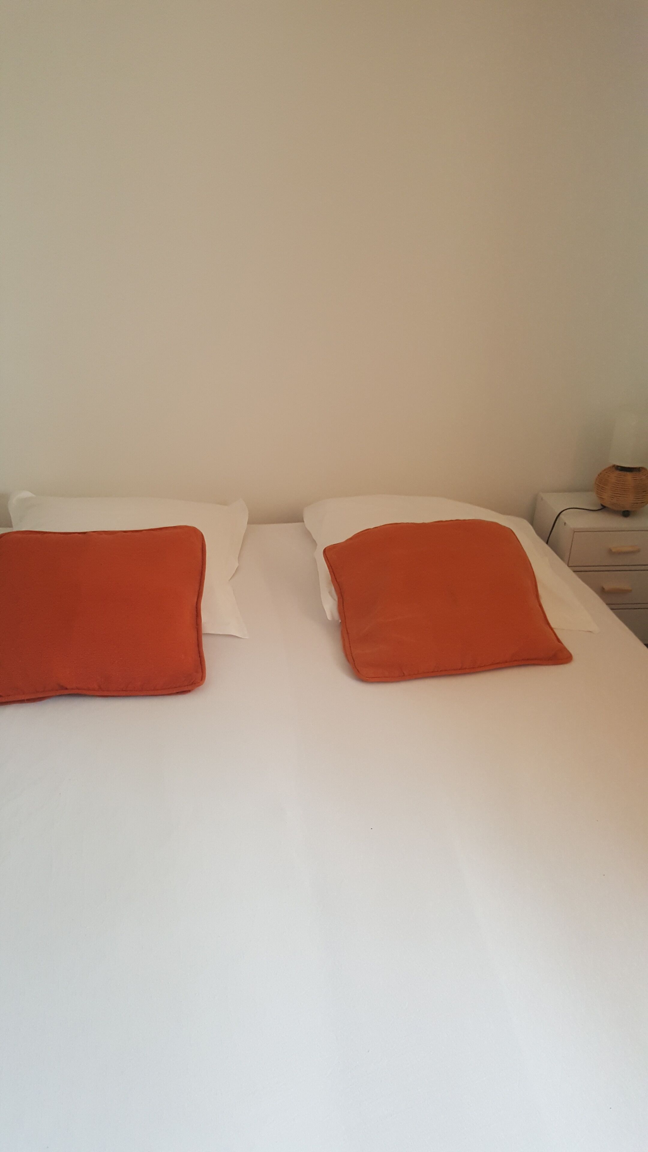A bed with white sheets and two red pillows.