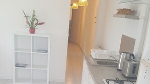 A modern kitchen with white cabinetry, a built-in oven, a sink, and a countertop with a toaster. There is a potted plant on a white shelf and a hallway leading to another room.