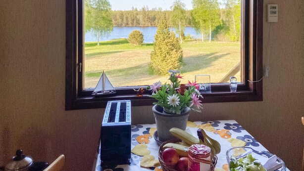 A room with a window view of a lake, a table with a floral tablecloth, and a small sailboat model.