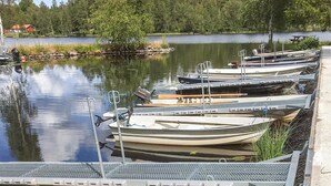 A row of small boats docked at a pier with a calm lake and trees in the background.