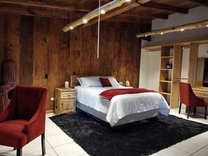 Un dormitorio con pared de madera, una cama con edredón blanco y rojo, una silla roja, una mesita de noche de madera y un escritorio con una silla.