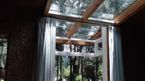 A room with a skylight, a red chair, and a view of a garden with a treehouse. - Asgard Resort (Santiago Sacatepéquez)