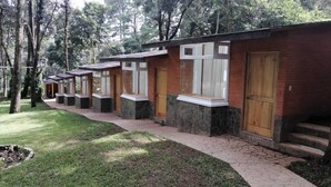 A row of stone and brick buildings with large windows and wooden doors, set in a wooded area. - Asgard Resort (Santiago Sacatepéquez)