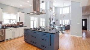 A modern kitchen with a central island, stainless steel appliances, and pendant lighting. - Eclectic, Stylish, and Cozy Milwaukee Home! (Milwaukee)