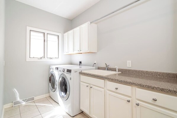 A laundry room with a washing machine, a sink, and cabinets.