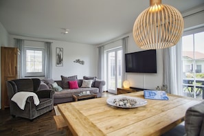 A modern living room with a grey sofa, wooden coffee table, and a large TV on the wall.