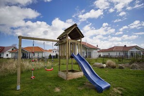 A playground with a swing set and a slide, surrounded by houses with red roofs.
