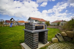 A backyard with a brick barbecue grill, a slide, and houses in the background.