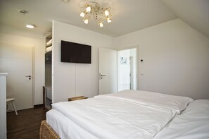 A bedroom with a large bed, a television mounted on the wall, and a chandelier. - Villa Morgensünn - House in an idyllic location with sauna, terrace and garden - (Trent)