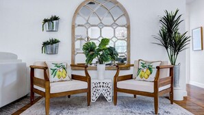 Une pièce comprenant deux chaises en bois avec des coussins, une table blanche et une grande fenêtre ornée d’un motif géométrique.