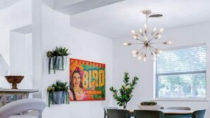 Un espace repas moderne avec un plancher en bois, une table centrale entourée de chaises, un luminaire suspendu et un tableau accroché au mur.