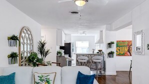 Un salon moderne avec un canapé blanc, un ventilateur de plafond et une cuisine en arrière-plan.