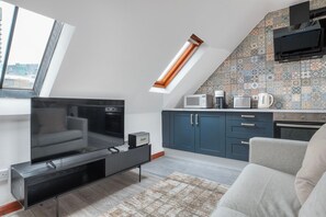 A modern loft apartment with a living area featuring a flat-screen TV, a sofa, and a dining area with a kitchen.