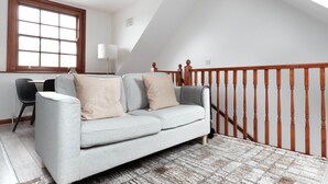 Ein modernes Wohnzimmer mit grauem Sofa, einer Holztreppe und Blick ins Freie.