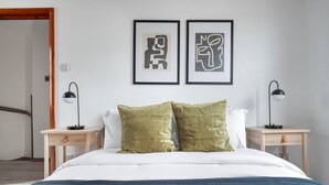 Ein Schlafzimmer mit einem Bett, zwei Nachttischen, zwei Lampen und zwei abstrakten Kunstwerken an der Wand.