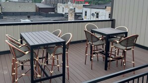 Eine Dachterrasse mit Tisch und Stühlen, einem roten Schild und Gebäuden im Hintergrund.