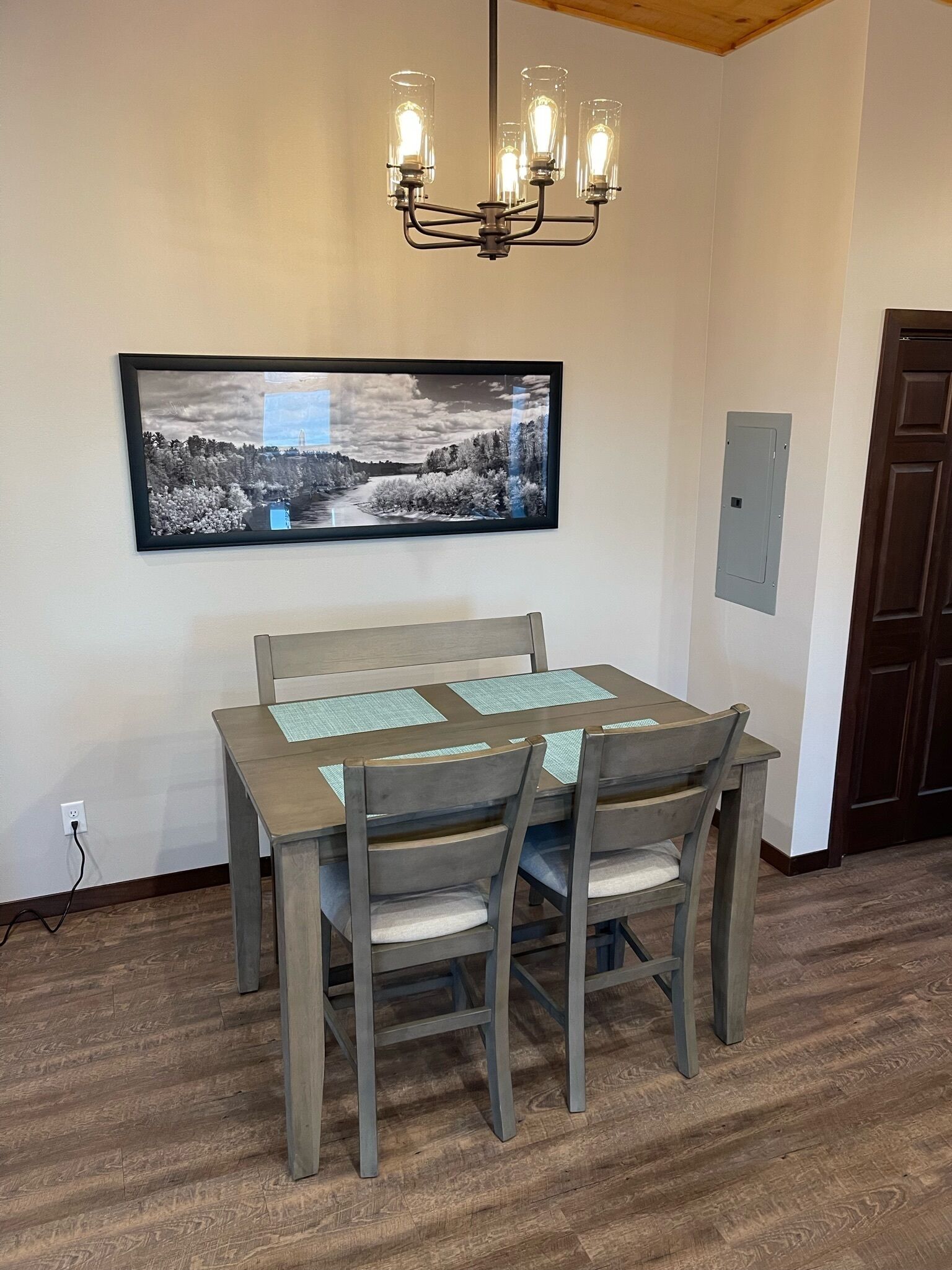 A dining room with a table and chairs, a chandelier, and a framed picture on the wall.