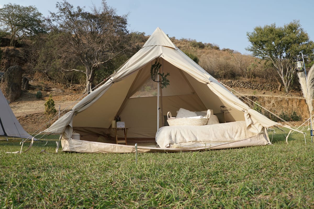 A tent with a bed inside, surrounded by grass and trees.