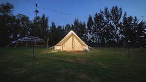 Una tienda grande de color beige con un pico triangular, rodeada por un campo de hierba y árboles.