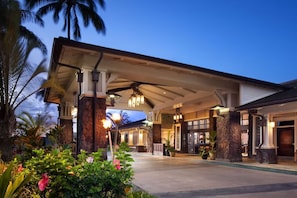 A hotel entrance with a covered walkway, palm trees, and well-lit interior.