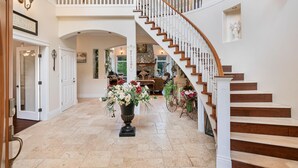 A spacious foyer with a grand staircase, a large vase of flowers, and a welcoming sign.