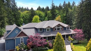 A two-story house with a grey roof, surrounded by a lush green forest.