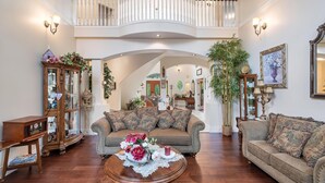 A spacious living room with a high ceiling, a grand staircase, and a large arched doorway leading to another room.