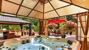 A hot tub with multiple jets, surrounded by a pergola with a roof, outdoor furniture, and potted plants.