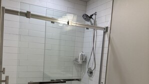 Ein modernes Badezimmer mit Duschkabine aus Glas, weißer Toilette und Waschtisch aus Holz.
