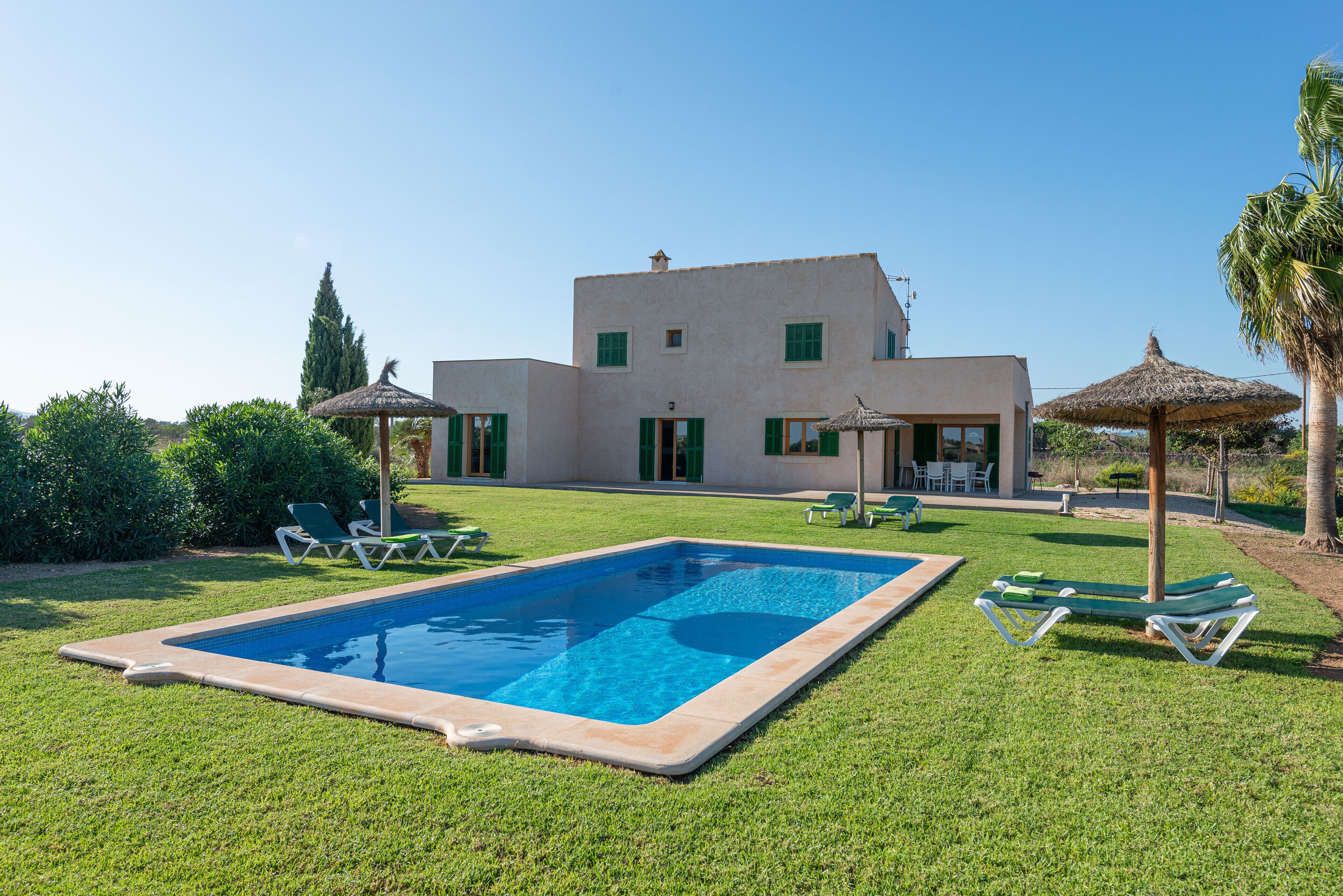 Una piscina con sillas de descanso, una casa de techo plano y un cielo despejado.