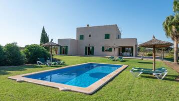 Una piscina con sillas de descanso, una casa de techo plano y un cielo despejado.