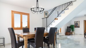 Een eetgedeelte met een houten tafel en stoelen, een kroonluchter en een trap met een leuning.