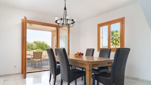 Een eetgedeelte met een houten tafel en zes stoelen, een kroonluchter en een uitzicht door een open deur op een terras.