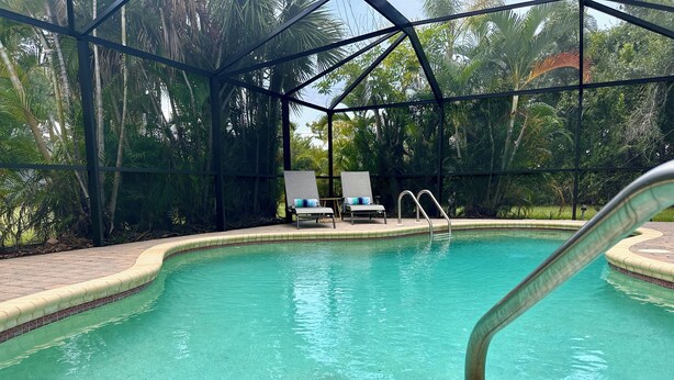 A clear swimming pool with a tiled edge, a metal pool ladder, and two lounge chairs with cushions.
