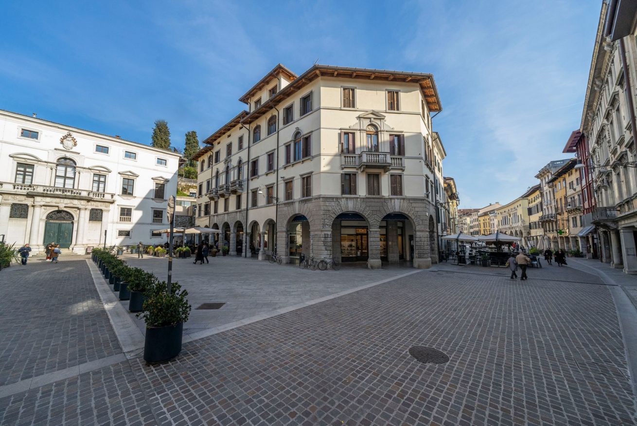 A historic square with cobblestone pavement, classical architecture, and a central building with a balcony.