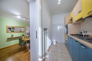 Una cocina con estufa, lavamanos y armarios, un comedor con sillas y mesa, y un pasillo con radiador.